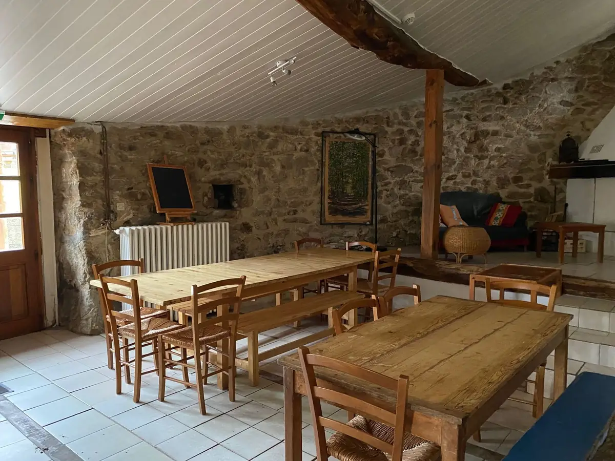 Une salle à manger aux murs de pierre, grandes tables en bois et chaises paillées